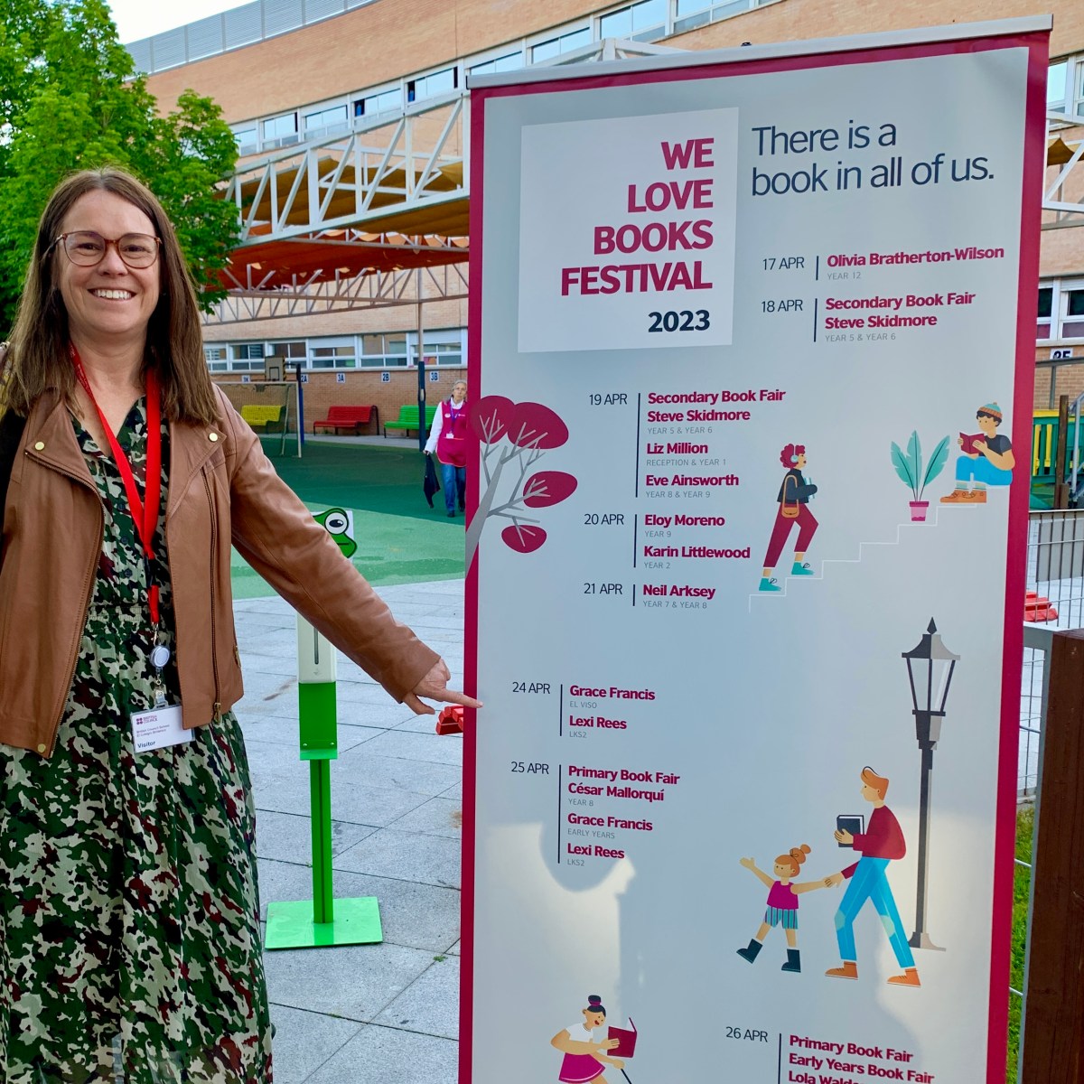 Lexi standing next a sign for the "We love books" festival in Madrid pointing at her name on the schedule